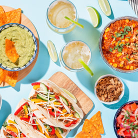 Mexican food table with traditional dishes. Chili con carne, tacos, tomato salsa, corn chips with guacamole. Mexican feast in hard light on blue color background, top view