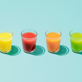 Four glasses of different colored juice on a colorful background.